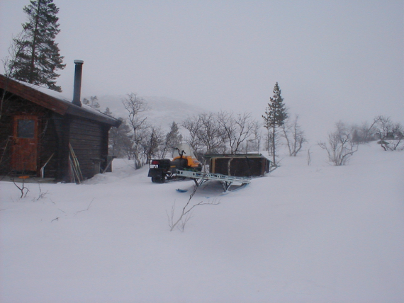Det er vinter, snøskuter ved siden av en hytte.