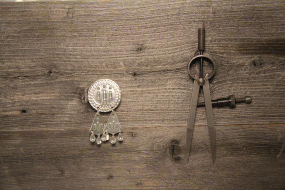 Foto av en rund sølvknapp med mønster av tre lys.