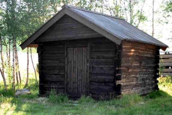 Stabbur på grønt gress med løvtrær i bakgrunnen.