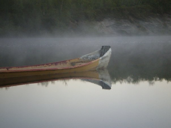 Elvebåt i blikkstille vann, i tåka.