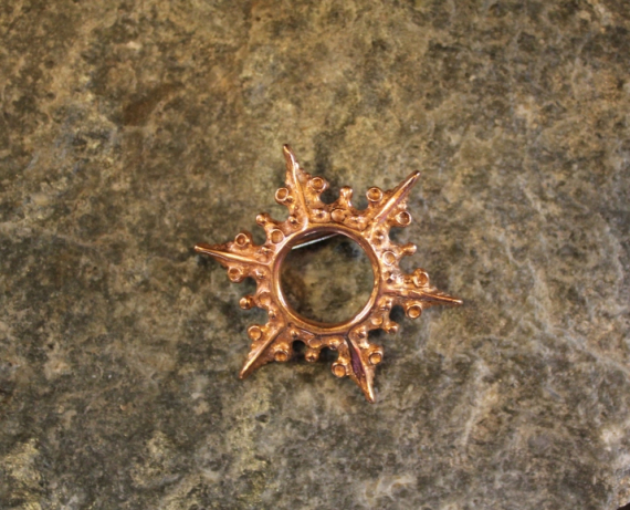 Foto av en messingbrosje med samisk solmønster.