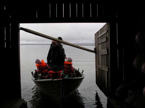 En voksen og tre barn kommer inn i et naust med båt.