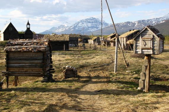 Foto av gamle tømmerhus med vannheis og sjåer mellom husene.